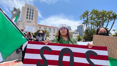 Karina Avila (center) holds an upside down American flag with the letters "SOS" on it at the "No Kings" Day protest in downtown San Diego on June 14, 2025. "No Kings" Day is part of a nationwide demonstration against the policies of the Trump administration. 