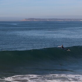A surfer floats along the top of a wave at Imperial Beach on Monday, Dec. 2, 2024.