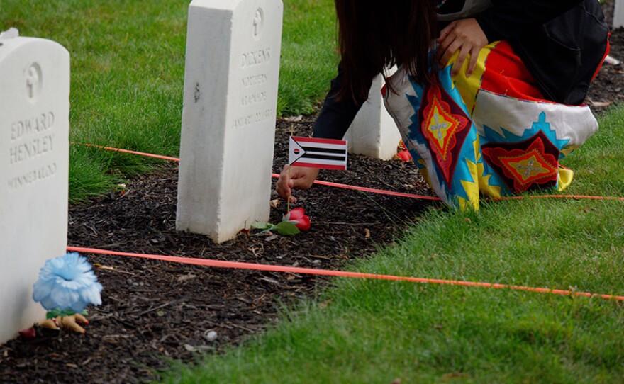 Loveeda White places an Arapaho flag at the base of Little Chief/Dickens Nor's headstone in the Carlisle Indian Cemetery