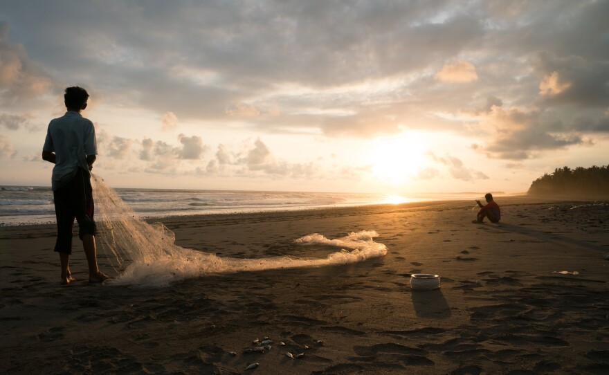Two men rest on a beach in Bali, Indonesia, where human bones were found in the 1990s. More bones have been recovered there since then, which villagers have reburied. The site is believed to be one of the mass graves for victims of the anti-communist atrocities.