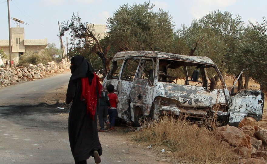 A woman walks past a wrecked van near the northwestern Syrian village of Barisha. Local residents and medical staff told NPR that noncombatant civilians who were in the van were injured and killed last year the night of the U.S. raid on the compound of ISIS leader Abu Bakr al-Baghdadi. The military says the men were combatants but found no weapons.