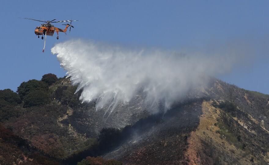 A helicopter drops water over a part of the Oakland Hills in Oakland, Calif., Tuesday, Sept. 26, 2017. 