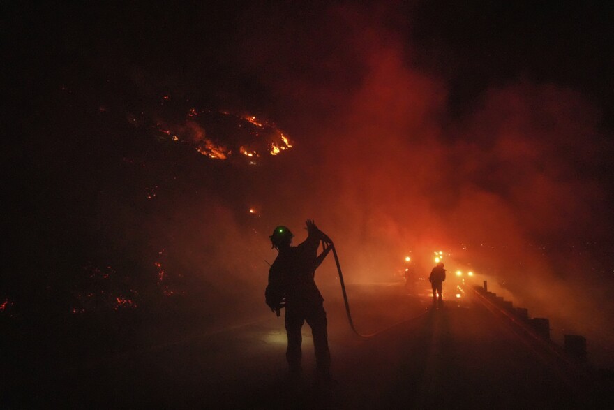 Two firefighters roll up a fire hose during the Lilac Fire in Bonsall, Calif., Tuesday, Jan. 21, 2025.