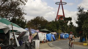 A cyclist passes the row of tents and tarps along the Santa Ana riverbed near Angel Stadium in Anaheim, Calif., Thursday, Sept. 14, 2017. 