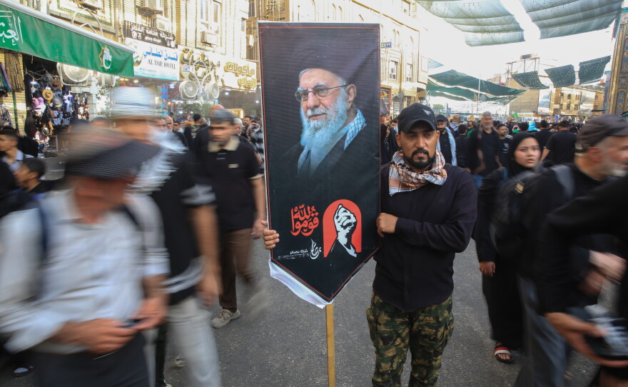 A man carries a large banner featuring a portrait of Iran's slain Supreme Leader Ali Khamenei amid crowds of pilgrims on a street in Karbala during Arbaeen.