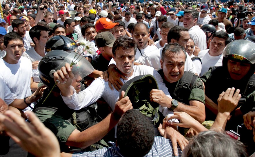 Opposition leader Leopoldo Lopez (dressed in white and holding a flower stem) is taken into custody in Caracas in February 2014. He is being held at a military prison outside the capital. He led protest rallies a year ago. The opposition is currently divided and weak.