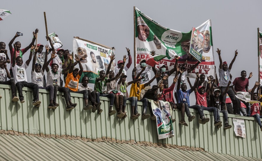 Supporters stand on a roof with placards and banners as they attend the final campaign rally of the Nigerian opposition leader Atiku Abubakar on Thursday in Jimeta, eastern Nigeria.