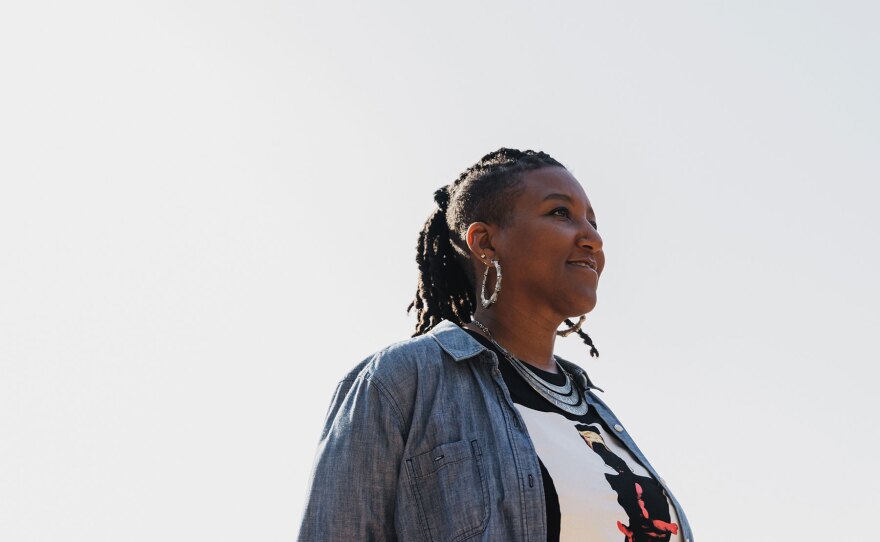 Hip hop artist Miki Vale stands against a white backdrop and looks off to the side.