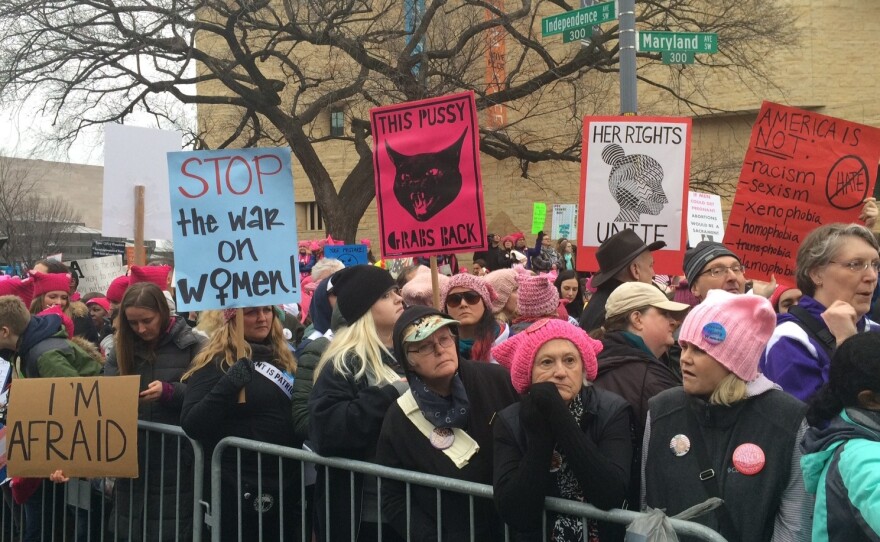 Marchers gather outside the National Museum of the American Indian, bearing signs protesting President Trump.