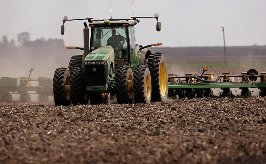 A green tractor that's planting corn moves across a brown dirt field in 2007 near Rochelle, Ill.