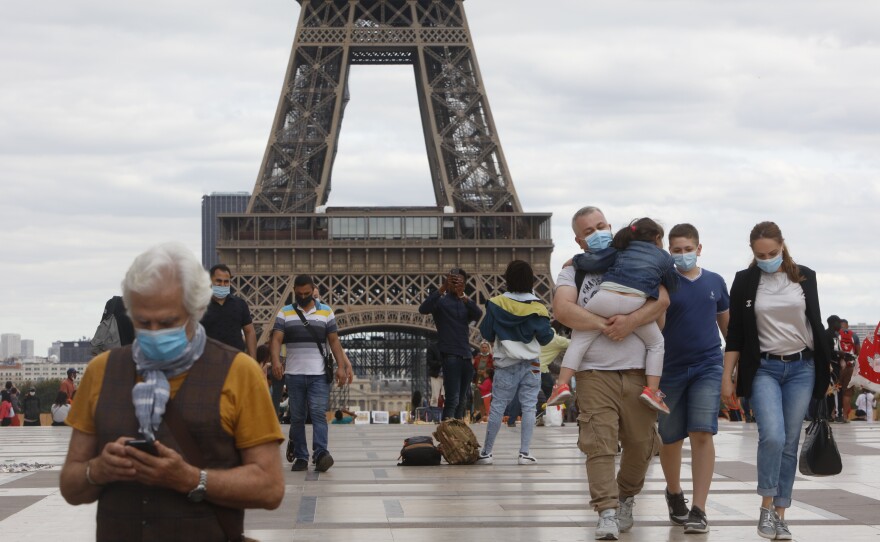 People wearing masks walk near the Eiffel Tower in Paris on Thursday, the same day that the government made masks mandatory in all the city's public outdoor spaces.