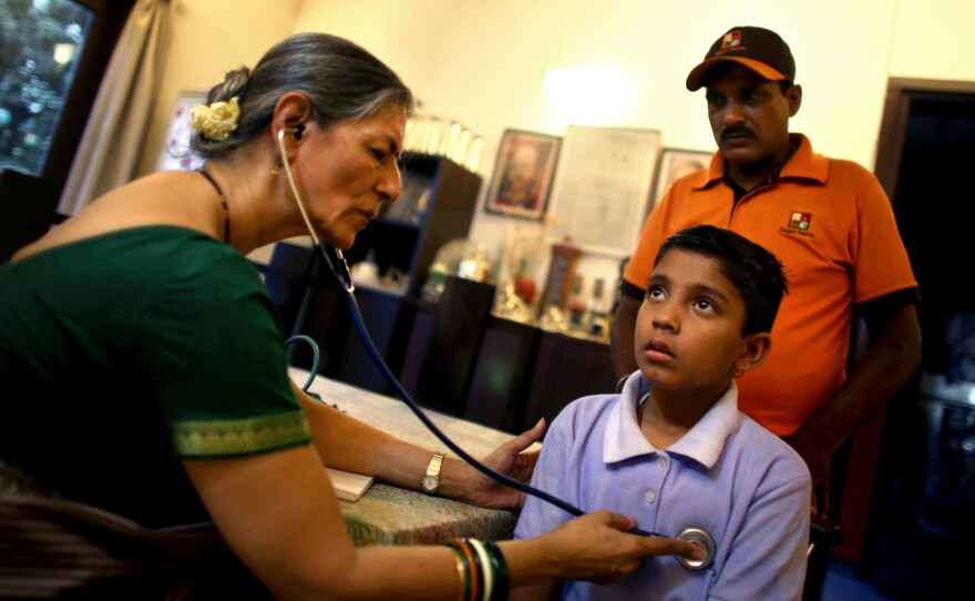 Dr. Gita Prakash (left), who runs a family clinic from her home in New Delhi, examines 10-year-old Sonu Kumar Chaudhary as his father, restaurant deliveryman Dilip Kumar Chaudhary, looks on. Prakash sees more and more cases of illness caused by the city's polluted air.