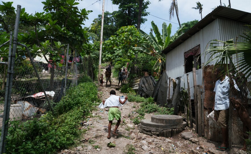 A boy runs up a dirt street in the Sabama settlement of Port Moresby, where people live in homes built out of bush material, lumber and corrugated metal.