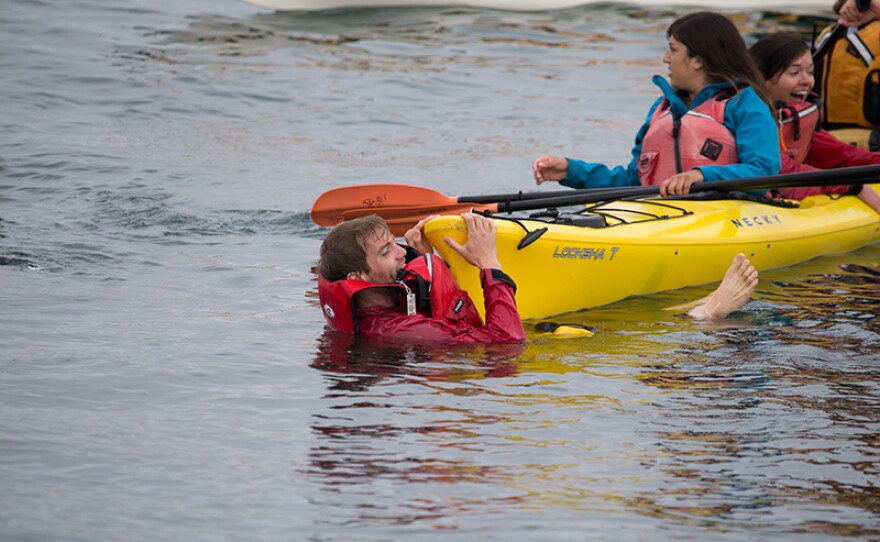 Filmmaker Tom Mustill and Charlotte Kinloch holding onto other whale watchers’ kayak after surviving the whale breaching onto them.