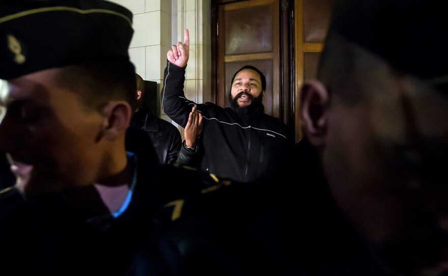 French comedian Dieudonne M'Bala M'Bala, center, gestures as he exits the courtroom after his trial in Paris last Wednesday. He was ordered to pay $37,000 for condoning terrorism. His lawyer argues he was denied the same freedom of expression that the satirical magazine Charlie Hedbo received.