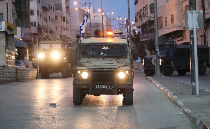 Israeli forces drive armored vehicles down a road during a raid in Hebron early on Jan. 21. The Israeli military says violence has surged in the West Bank since Oct. 7.