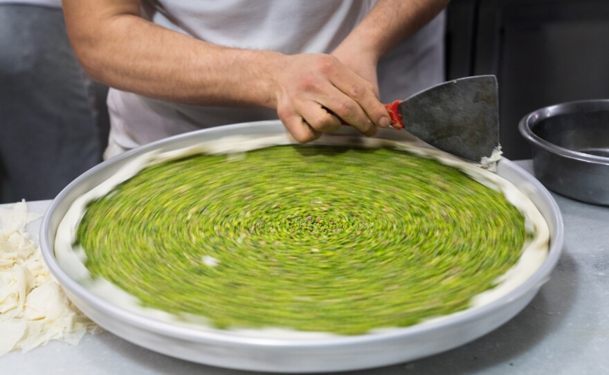 A baker fine-tunes the edges of a pan of baklava before it is covered with pastry.