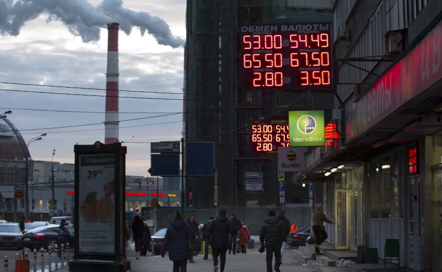 People walk past a display with currency exchange rates in Moscow on Wednesday. Falling oil prices have contributed to a number of economic problems, including a currency that has fallen from 35 rubles to the dollar this summer to more than 50 rubles to the dollar now.