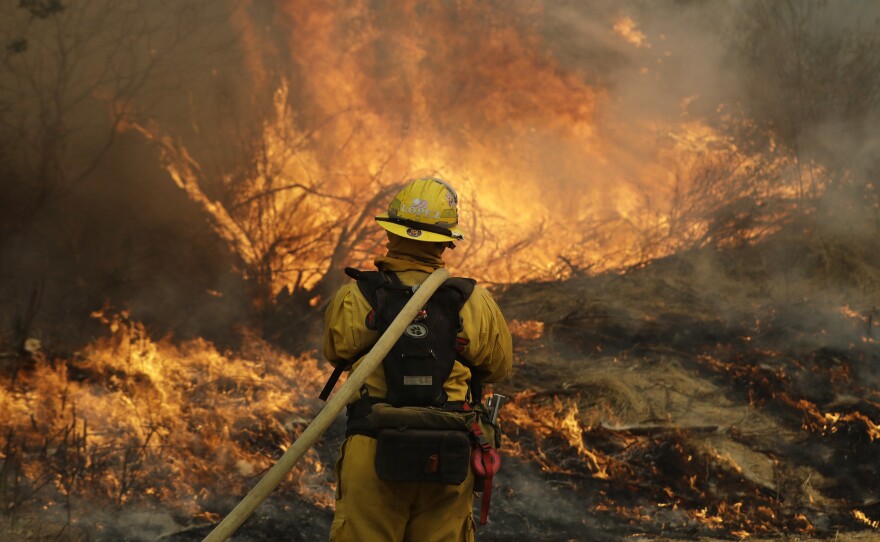 Fresno firefighter Peter Lopez holds a water hose as he monitors a backburn while fighting a wildfire in Glen Ellen, Calif.