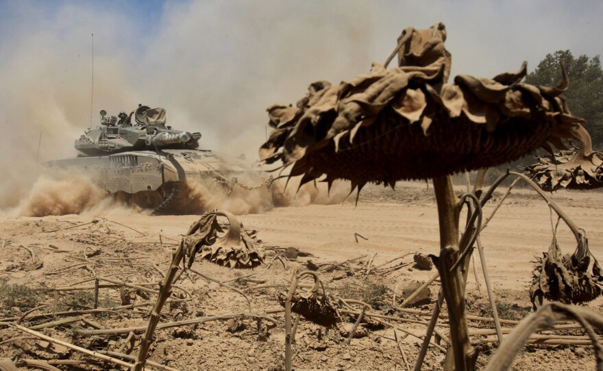 An Israeli tank drives past a field of sunflowers along the border between Israel and the Gaza Strip as they pull out from the Gaza Strip Sunday. At least 10 people died in a strike outside a U.N. school in Gaza shortly after Israel confirmed it was withdrawing some troops from the war-torn area.