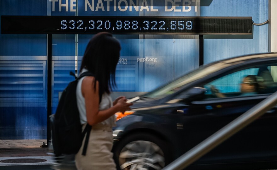Pedestrians walk past a poster and electronic billboard about the national debt displayed ain street in Washington, D.C., on July 5, 2023. The U.S. last had a budget surplus in 2001. Since then it's seen its deficits surge.