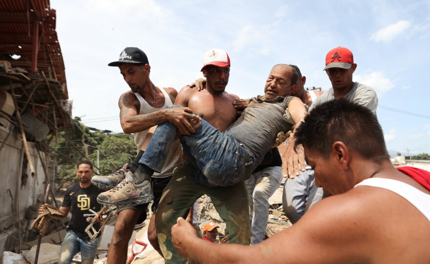 Neighbors carry a man rescued from the rubble of a collapsed building the day after earthquakes struck La Guaira, Venezuela, Thursday, June 25, 2026.