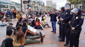People holding signs sit on the ground in front of police officers in downtown San Diego, May 27, 2016.