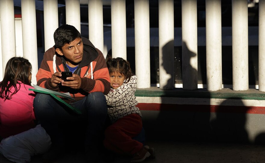 A migrant and his children wait to hear if their number is called to apply for asylum in the United States, at the border in Tijuana, Mexico.