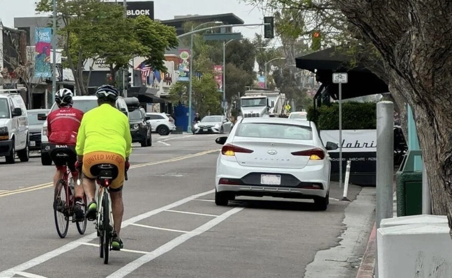 Two cyclists ride past a car parked in the bike lane of 30th Street in North Park.