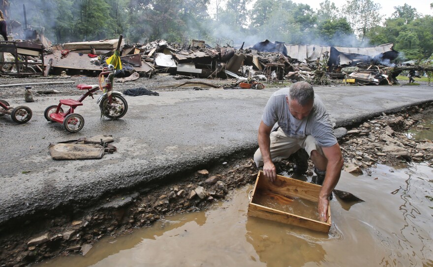 Mark Lester cleans out a box with creek water as he cleans up from severe flooding in White Sulphur Springs, W. Va., on Friday.