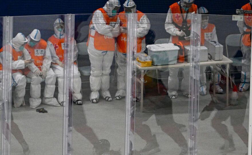 Hockey players are reflected in the safety barrier around the rink as medical personnel wearing personal protective equipment keep watch at the Beijing 2022 Winter Olympic Games.