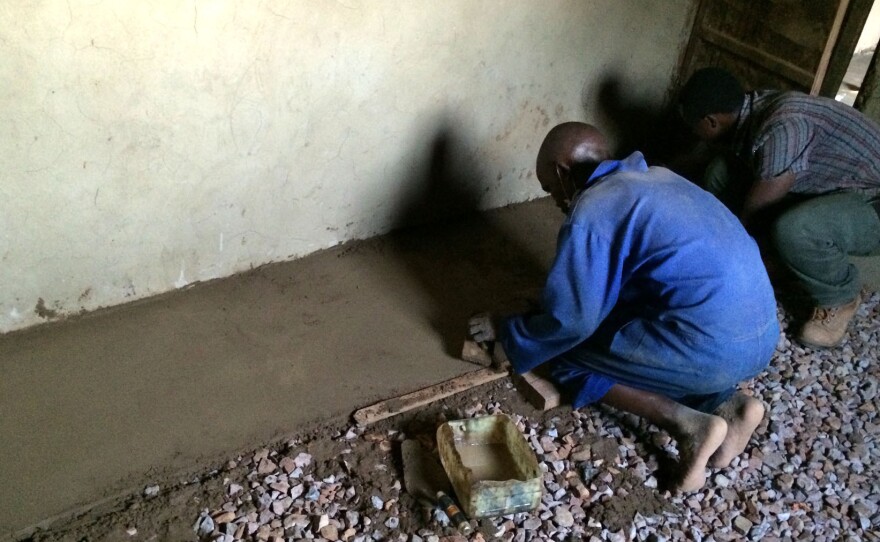 Gravel helps keep the floor level and prevents moisture from seeping up. The floor installers are Jean Pierre (left), a mason, and Daniel Shenyi, operations manager for EarthEnable.