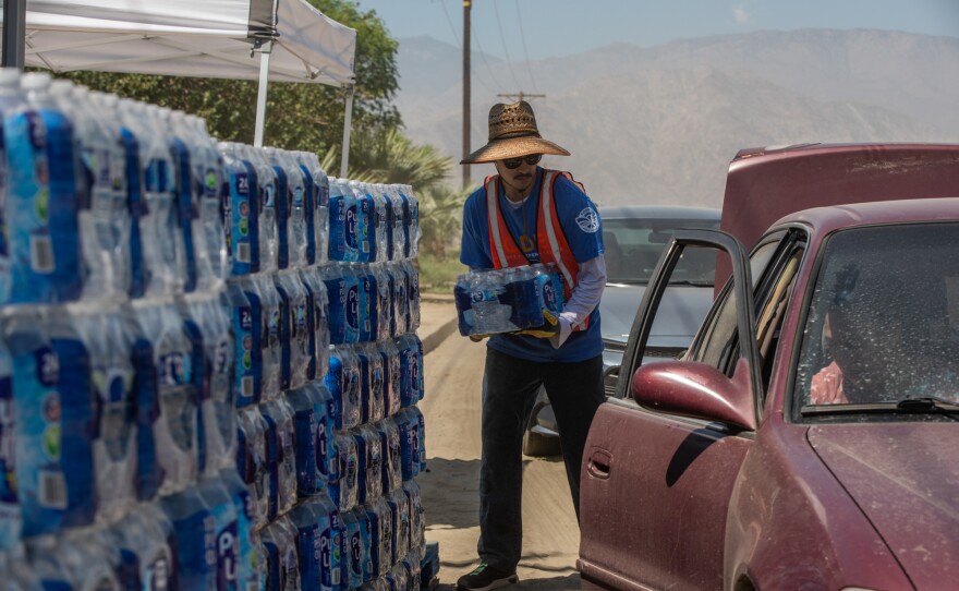 A member of TODEC loads a crate of bottled water into a resident's vehicle outside Oasis Mobile Home Park in Coachella Valley on Aug. 24, 2023.