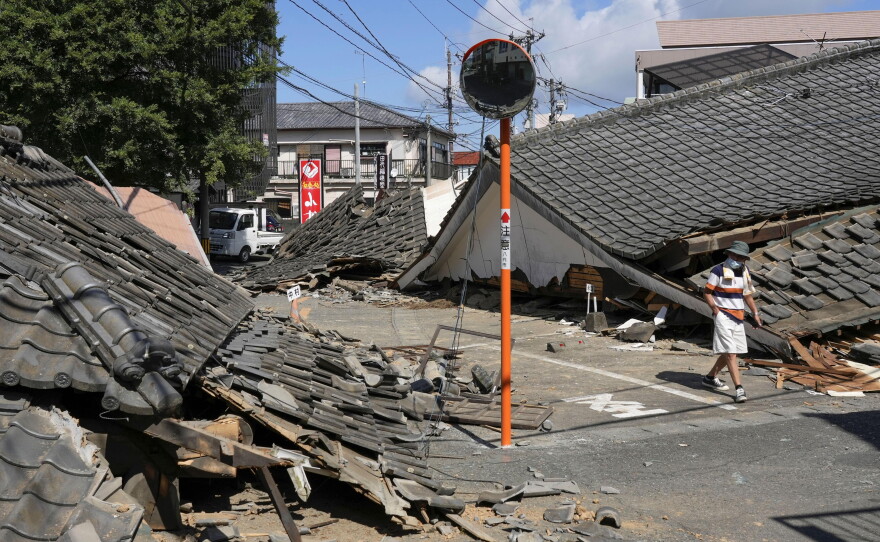 A person walks past the houses collapsed in an earthquake in Yatsushiro, Kumamoto Prefecture, southern Japan, Friday, July 31, 2026.