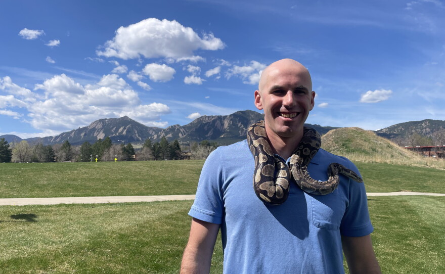 Jack Gugel stands with a pet python around his neck in front of the Flatirons, the iconic slabs of sandstone that help make Boulder a climber's paradise.  Gugel has been researching how pythons are able to rapidly increase the size of their hearts.