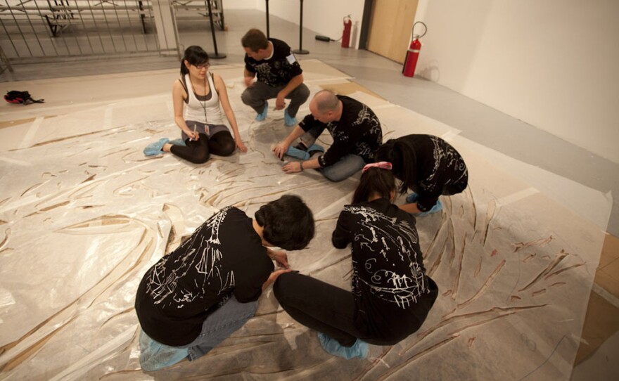 Before the explosion, volunteers help prepare the enormous canvases with cardboard stencils.