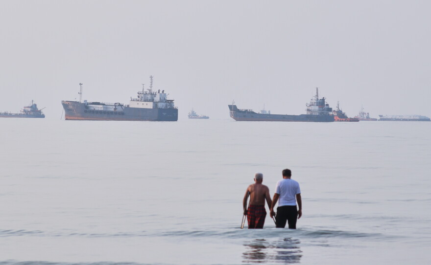 Two men wade in the waters of the Strait of Hormuz with vessels anchored in the background, off Bandar Abbas, Iran, Sunday, July 12, 2026.