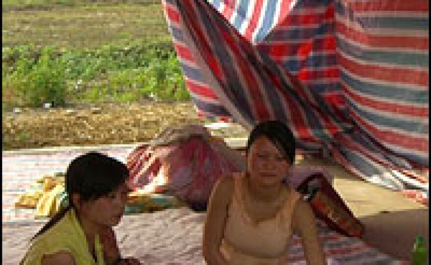 Sisters Chen Huayu (left, holding her 3-year-old daughter) and Chen Xiaoli sit in what counts as their new home — a makeshift tent that runs for hundreds of yards along the main road in the city of Shifang.