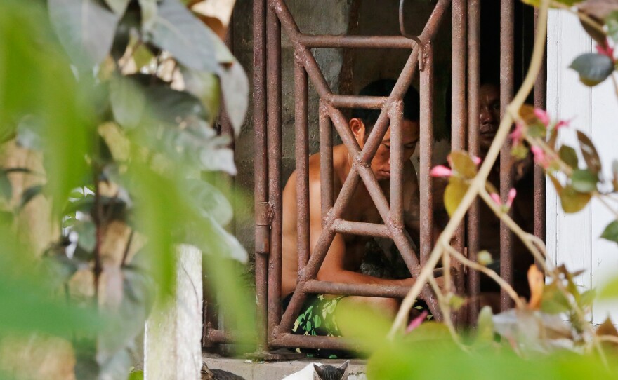 Thai and Burmese fishing boat workers sit behind bars inside a cell at the compound of a fishing company in Benjina, Indonesia. The imprisoned men were considered slaves who might run away. They said they lived on a few bites of rice and curry a day in a space barely big enough to lie down, stuck until the next trawler forces them back to sea.