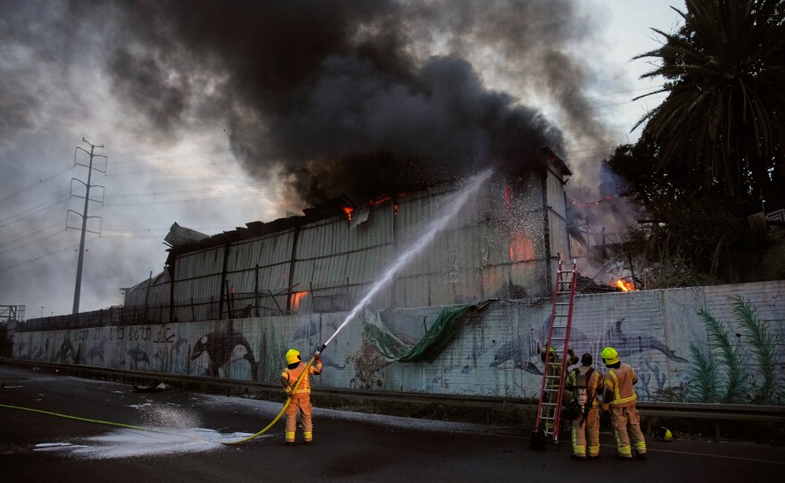 Firefighters try to extinguish flames at the site of a direct hit by an Iranian missile strike in Holon, central Israel, Friday.
