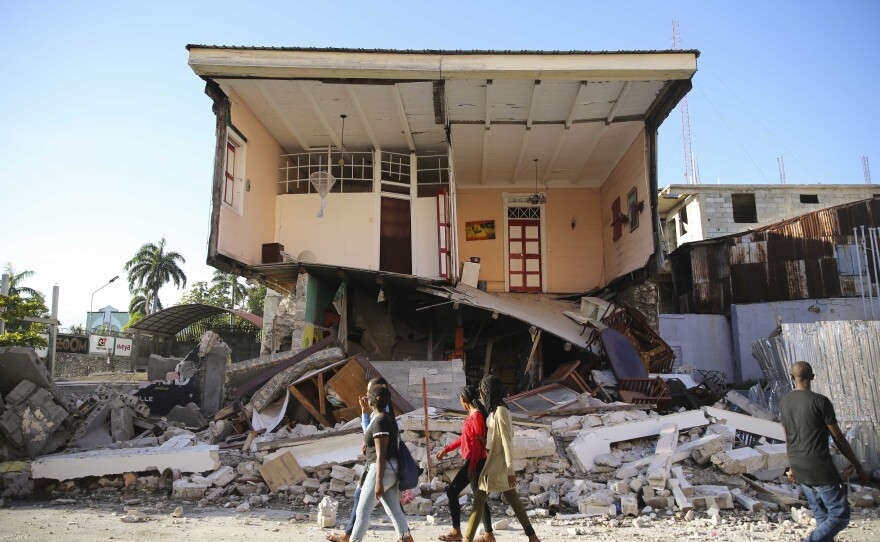 <strong>Sat., Aug. 14:</strong> People walk past a home destroyed by the earthquake in Les Cayes, Haiti.