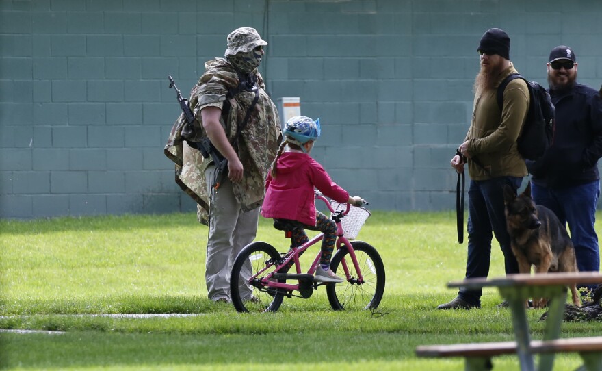 An anti-LGBTQ protester carries a semi-automatic rifle as he walks near the the "Pride in the Park" event in Coeur d'Alene.