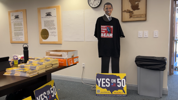 A cardboard cutout of Barack Obama sporting a shirt that reads "Don't poke the bear" in a room with "Yes on 50" signs and material.