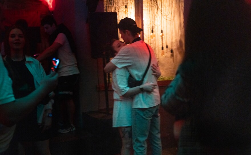 Two people dance together and kiss amongst the crowd.