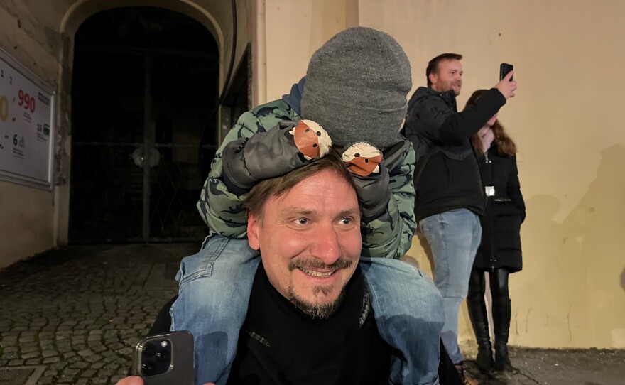 Salzburg resident Rene Watziker watches the Krampuses go by, but his four-and-a-half year-old son Valentin perched is too scared to look at them.