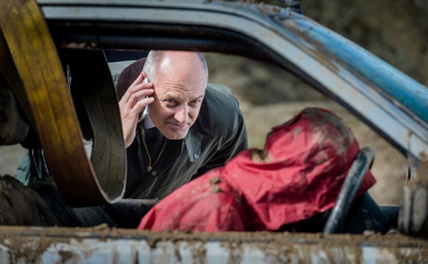 DC Ian Mitchell (David Prosho) stands in the quarry on the phone and looks through the car to find a dead body at the wheel.