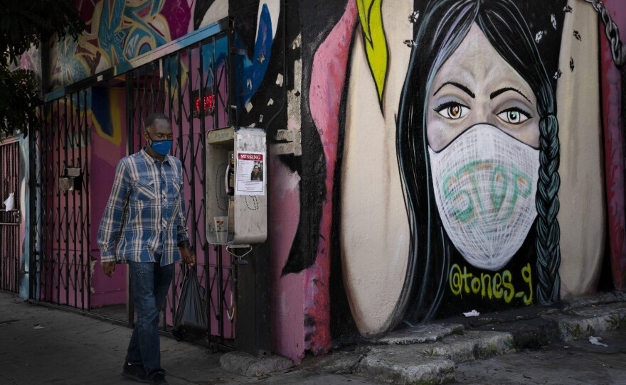 A man wearing a face mask walks past a mural Thursday, Oct. 1, 2020, in South Central Los Angeles. California's plan to safely reopen its economy will begin to require counties to bring down coronavirus infection rates in disadvantaged communities that have been harder hit by the pandemic. 