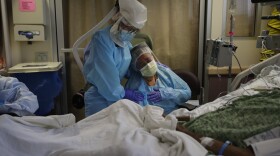 In this July 31, 2020, file photo, Romelia Navarro, right, is comforted by nurse Michele Younkin as she weeps while sitting at the bedside of her dying husband, Antonio, in St. Jude Medical Center's COVID-19 unit in Fullerton, Calif. 
