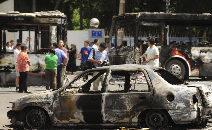 People walk past burned-out cars and buses in a street in Urumqi on July 6, 2009, following deadly rioting. The violence in Urumqi on July 5, 2009, involved thousands of people and triggered an enormous security crackdown across Xinjiang, where tensions have long simmered amid Uyghur claims of repressive Chinese rule.