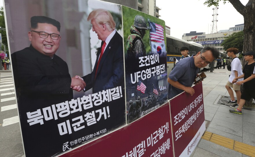 A photo of President Trump and North Korean leader Kim Jong Un is on display as a member of People's Democratic Party stands in opposition of military exercises between the United States and South Korea near the U.S. embassy in Seoul on Tuesday.